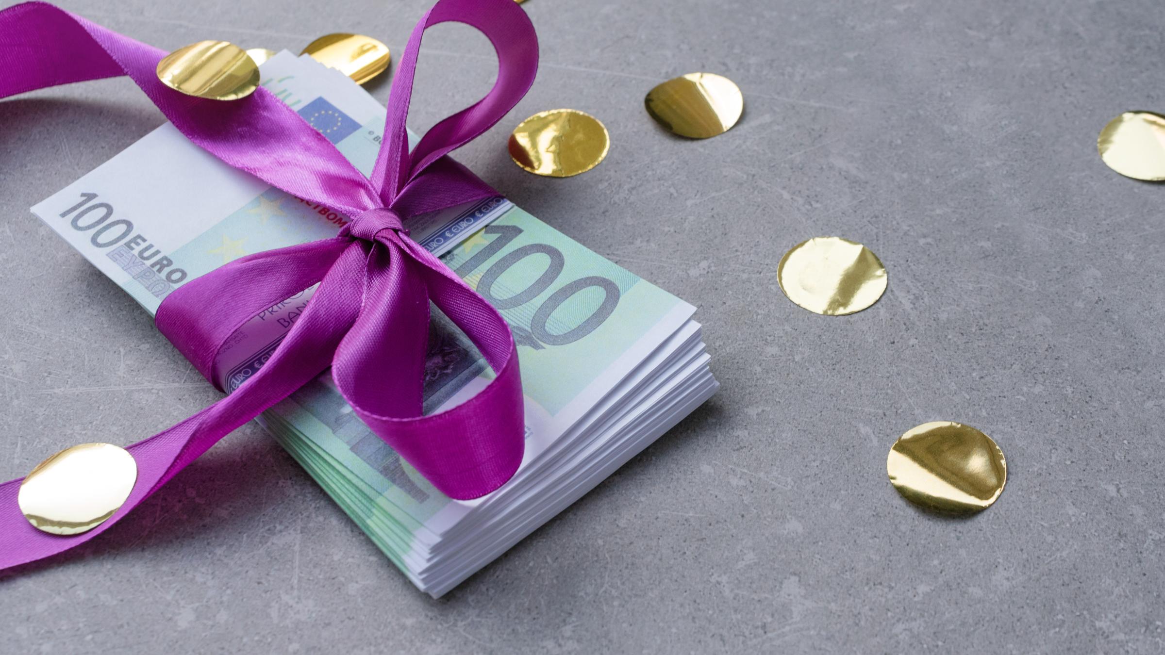 "WISO-Dokumentation: Ein Erbe vom Staat? 20.000 Euro für Jeden":  Ein Stapel 100-Euro-Scheine mit einer lila Schleife liegt auf einem grauen Untergrund.