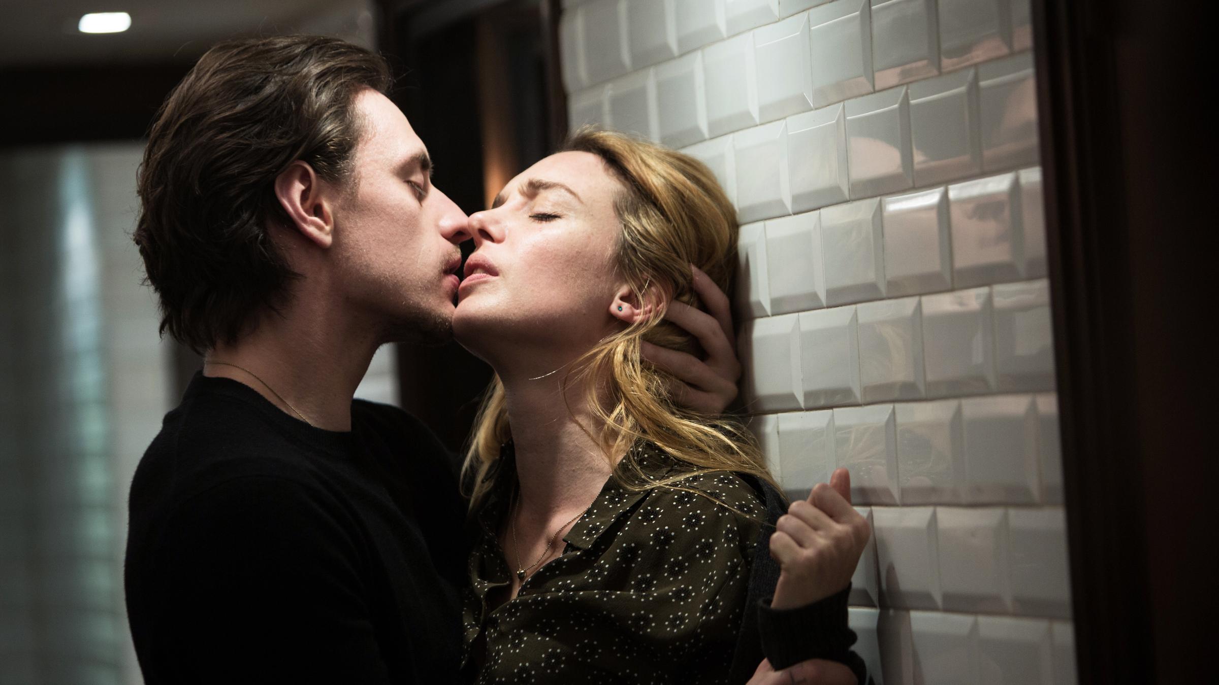 „Passion Simple“: Hélène (Lætitia Dosch) befindet sich mit dem Rücken zu einer Wand, die von oben beleuchtet ist. Alexandre (Sergej Polunin) steht ihr gegenüber und hält sie am linken Handgelenk fest, kurz bevor er sie küsst.