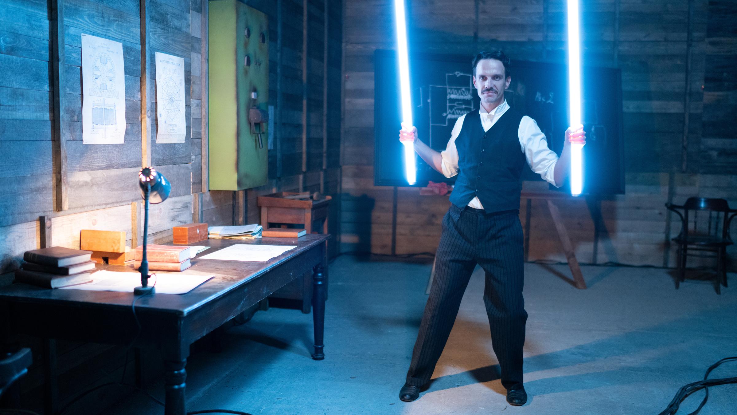 "Terra X: Nikola Tesla - Magier der Elektrizität": Spielszene: Nikola Tesla steht in seiner Werkstatt mit leuchtenden Röhren, die er wie Schwerter in der Hand hält.