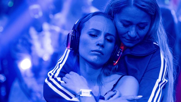 "Birthday Girl": Nahaufnahme: Cille (Flora Ofelia Hofmann) und Nanna (Trine Dyrholm) tanzen zusammen auf blau beleuchteter Tanzfläche. Nanna hält Cille mit geschlossenen Augen von hinten im Arm. Cille, die rot leuchtende Kopfhörer trägt, hat ihre Augen geistesabwesend gesenkt.
