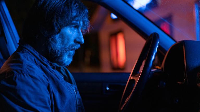 "Die Mörder meines Sohnes": Nahaufnahme: Leo Castaneda (Antonio de la Torre) sitzt mit angespanntem Blick am Steuer eines, bei einem Haus mit Leuchtreklame geparktem, Auto. Das Wageninnere ist blau ausgeleuchtet.