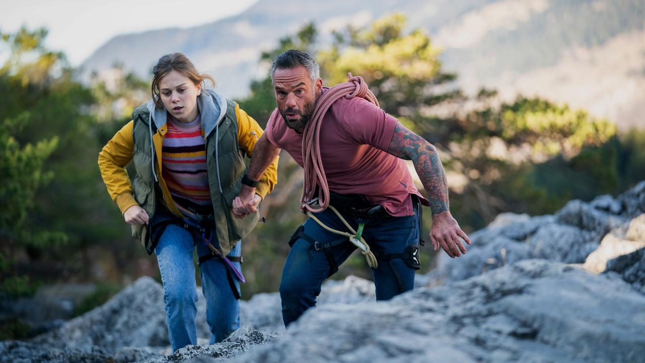 "Showdown in den Bergen": Paul (Philippe Bas) und Sara (Maïra Schmitt) laufen auf einem Felsen. Sie halten sich an den Händen.