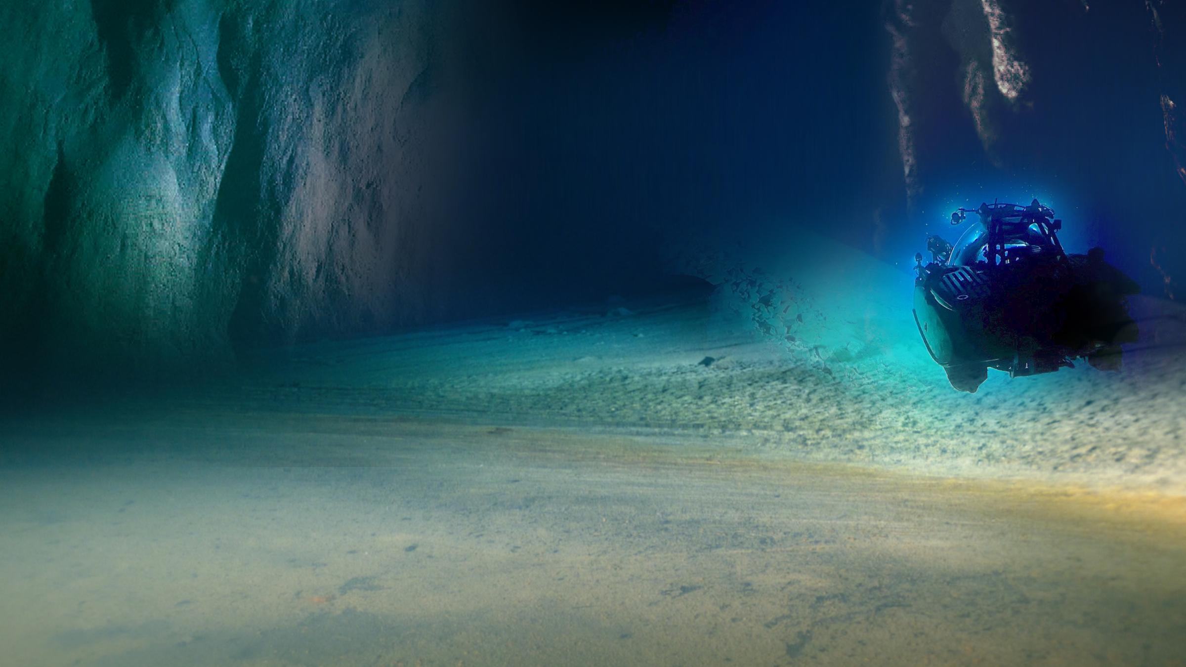 "Terra X: In unbekannten Tiefen" Blick auf türkis und blau leuchtende Felswände und einen Strand unter Wasser. Ein Tauchboot untersucht den Meeresgrund, in denen Bakterien aus früheren Phasen des Lebens vermutet werden.