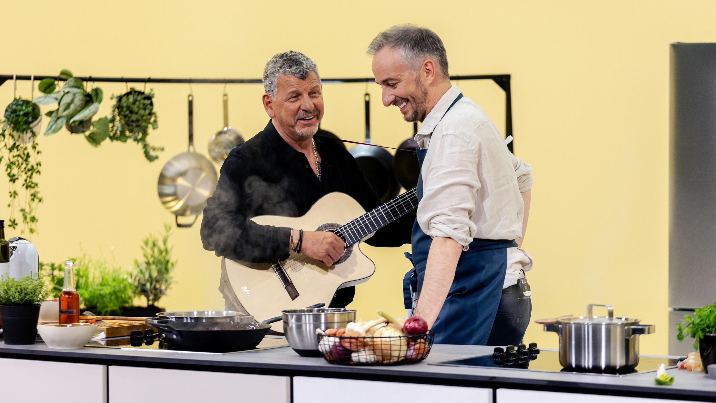 "Böhmi brutzelt": Semino Rossi und Jan Böhmermann in der Küche von "Böhmi brutzelt". Semino Rossi hat eine Gitarre in der Hand. Jan Böhmermann steht am Herd. Beide lachen.