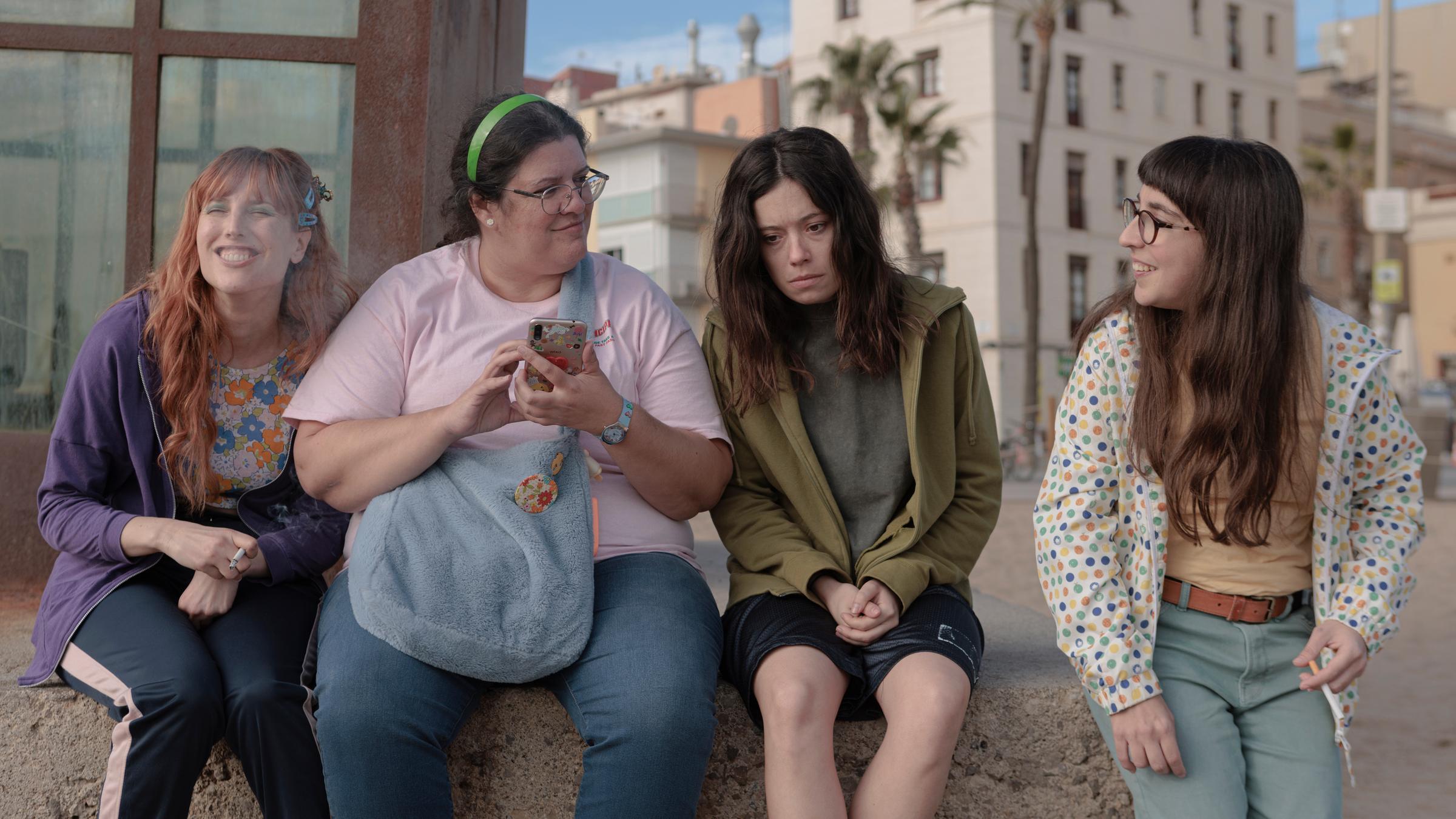 "Simple - Freiheit": Marga (Natalia de Molina), Àngels (Coria Castillo), Nati (Anna Castillo) und Patri (Anna Marchessi) sitzen zusammen auf einem Stein am Strand. Alle außer Nati lächeln.
