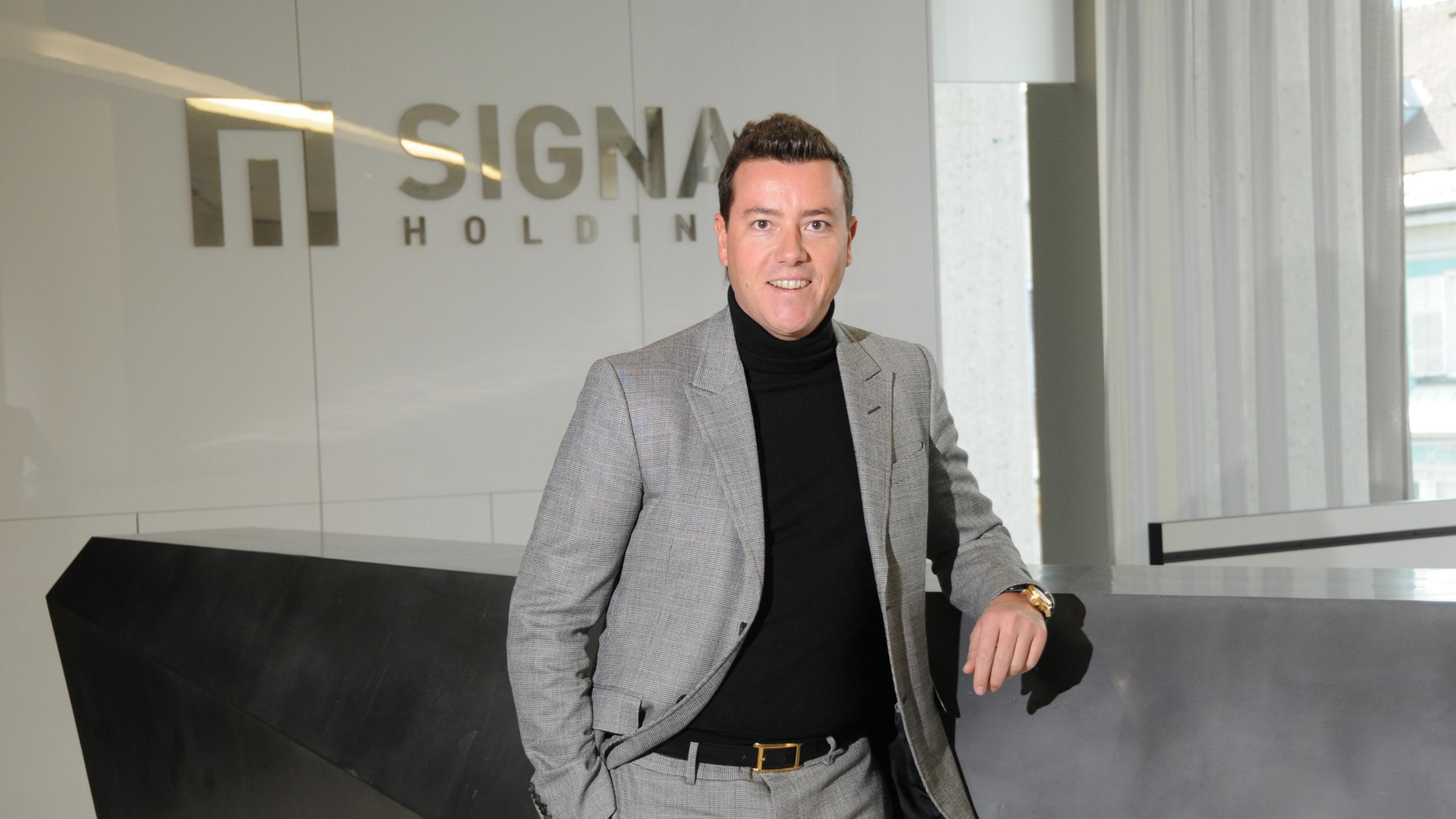 "WISO-Dokumentation: Spiel mit Milliarden – Die Benko-Pleite": Immobilien-Tycoon René Benko steht in schwarzem Rollkragenpulli und grauem Anzug in einem Raum vor dem Logo der Signa Holding. Er schaut gewinnend in die Kamera.