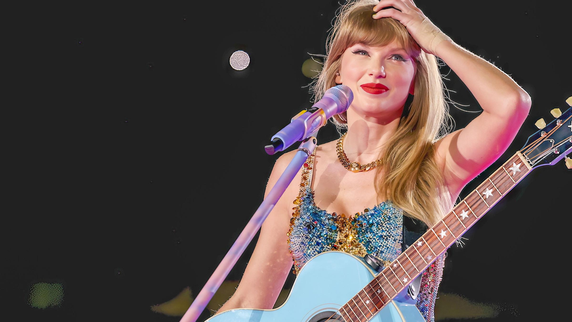 "The True Story of Taylor Swift": Taylor Swift steht mit Gitarre an einem Mikrofon. Sie lächelt und fasst sich an den Kopf.