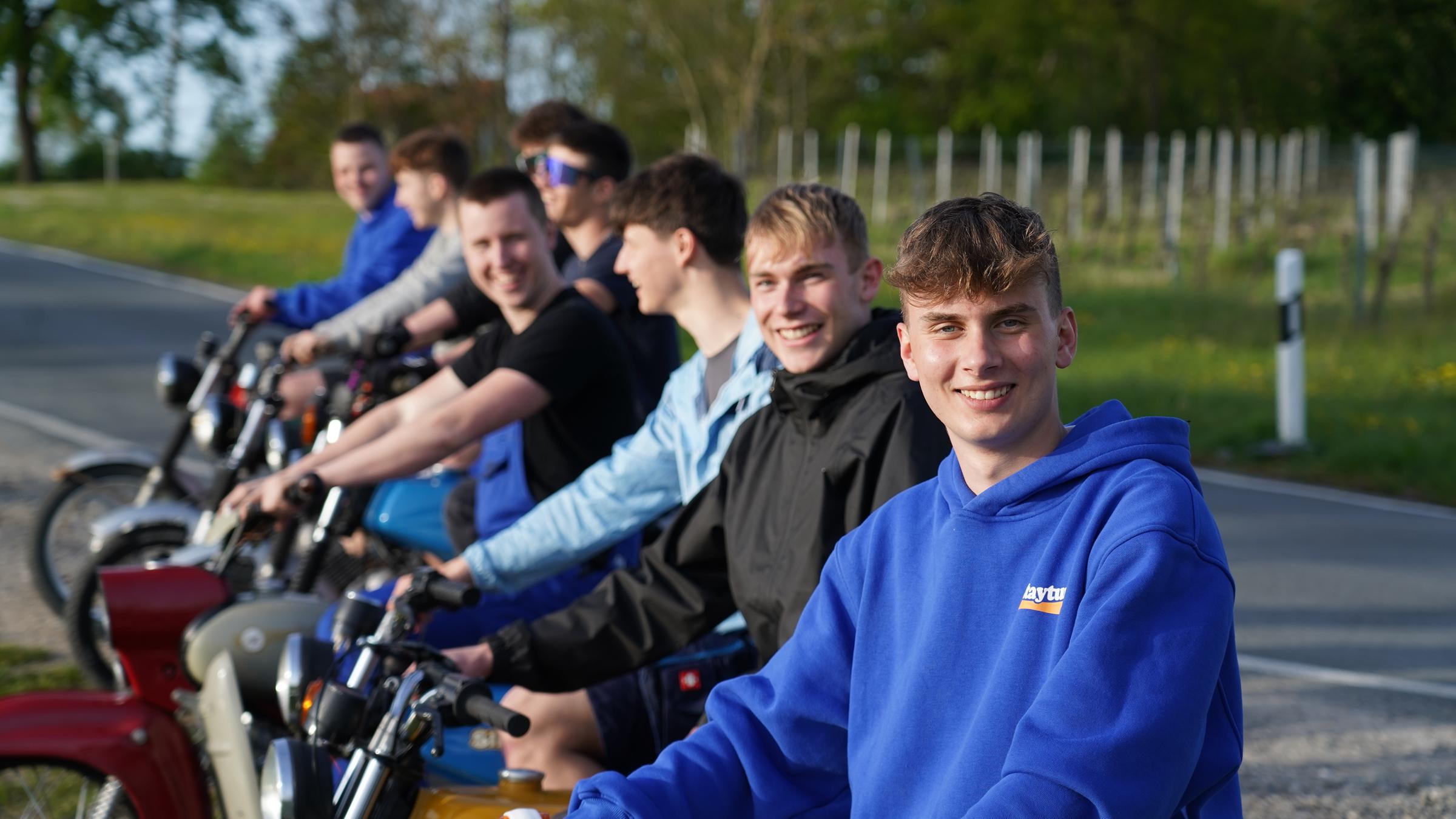 "ZDF.reportage: Jung im Osten – Wie wir wirklich leben": Jason aus Flurstedt und andere Jugendlichen sitzen auf Simson-Mopeds und lächeln in die Kamera. Im Hintergrund verläuft eine schmale Landstraße an der Bäume stehen.