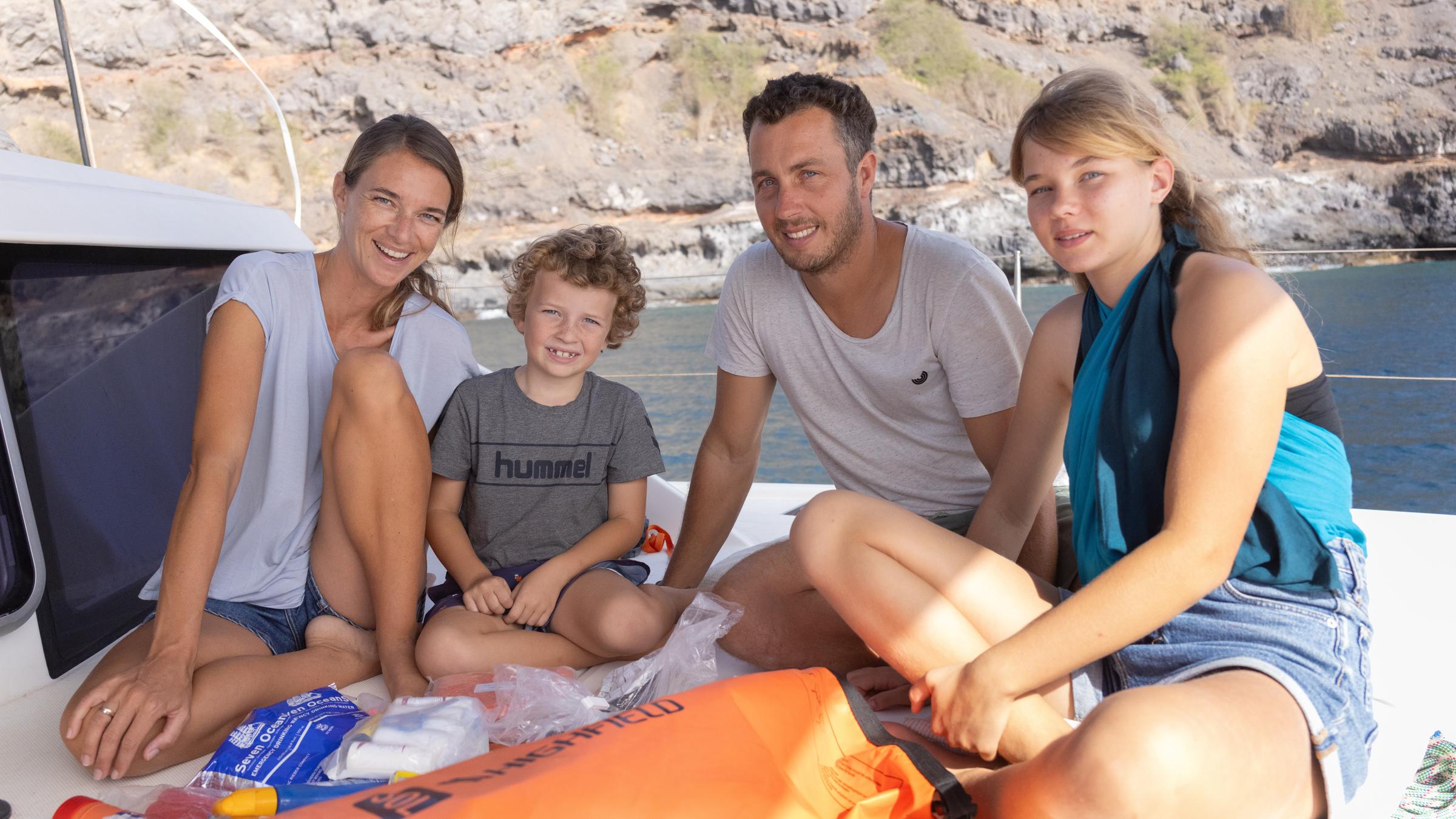 "Terra X: Abenteuer Freiheit - Auf Weltreise mit dem Segelboot": Mutter Natalie, Sohn Jonas, Vater Moritz und Tochter Sophie sitzen auf Deck und schauen in die Kamera. Dahinter liegt eine Felsenküste.