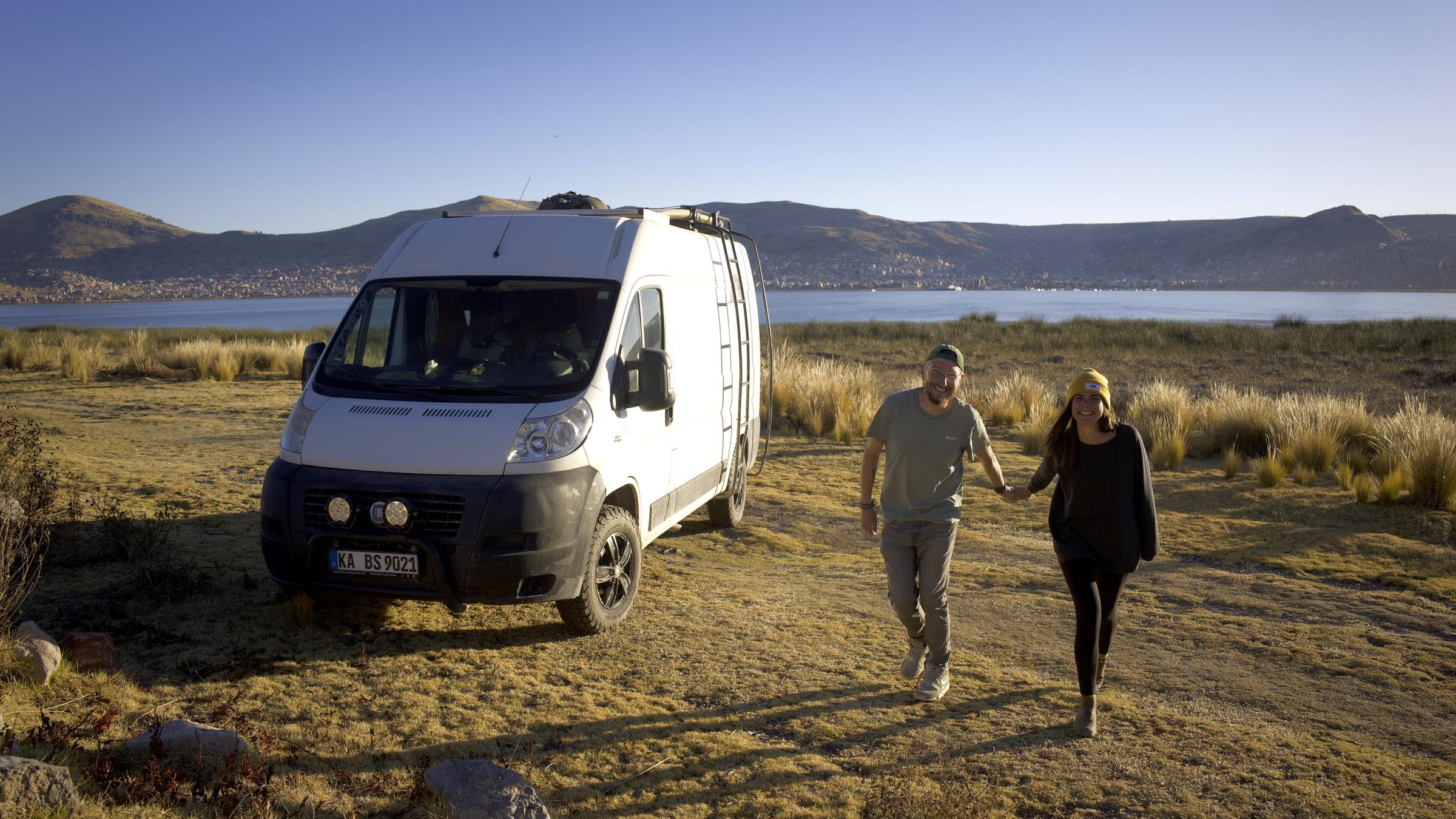 "Terra X: Abenteuer Freiheit - Vanlife in Südamerika": Sebastian und Svenja laufen im Sonnenschein Händchen haltend am Titicacasee. An der Seite steht ihr Wohnmobil.