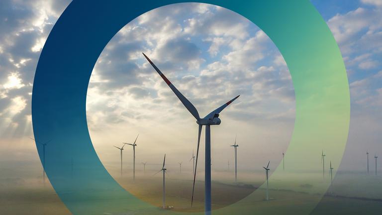 "planet e.: Green Deal - Kann Europa Klima?": Das Luftbild einer Drohne zeigt einen Windpark in Brandenburg: Die Windanlagen stehen in der Morgensonne, teils von Wolken verdeckt, in der in Frühnebel gehüllten Landschaft.