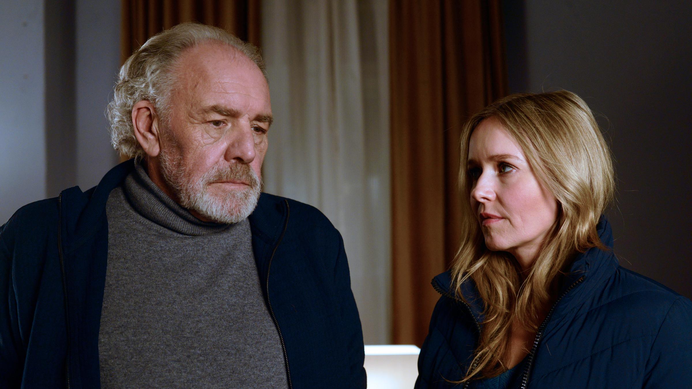 "Ein starkes Team - Tod einer Pflegerin": Lars Schellhorn (Christian Kohlund) und Linett Wachow (Stefanie Stappenbeck) stehen im Flur des Seniorenheims und unterhalten sich. Linett trägt eine grüne Jacke und offenes blondes Haar, Lars trägt einen dunklen Pullover und hat zurückfallendes graues Haar. Linett schaut zu Lars, dieser blickt zur Seite.