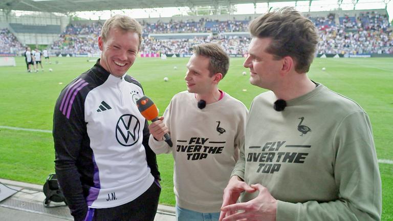 "heute-show spezial - Fußball - Ein Ball für zwei": Lutz van der Horst und Fabian Köster stehen am Spielfeldrand des Ernst-Abbe-Sportfelds in Jena und führen ein Gespräch mit Bundestrainer Julian Nagelsmann. Fabian Köster hält ein ZDF-Mikrofon in der rechten Hand.