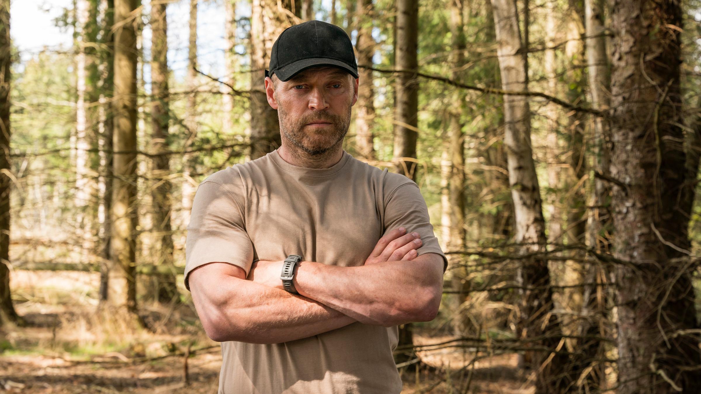 "Oxen - Staats-Affären": Niels Oxen (Jacob Lohmann) steht im Wald auf einer Lichtung. Er trägt eine Kappe und verschränkt die Arme vor der Brust.