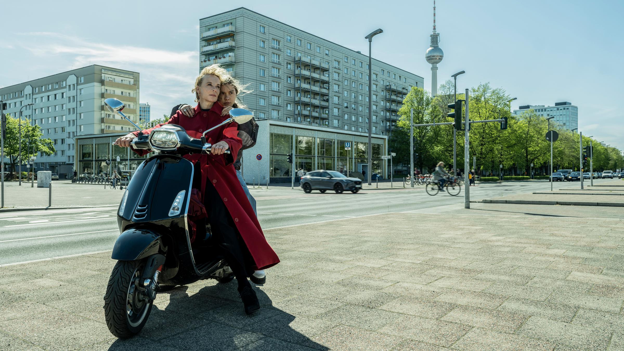 "RESET - Wie weit willst du gehen?": Flo Bohringer (Katja Riemann) und ihre Tochter Luna (Hannah Schiller) sitzen auf einem schwarzen Motorroller. Luna hält sich an den Schultern ihrer Mutter fest. Im Hintergrund stehen Wohnblöcke sowie der Berliner Fernsehturm.