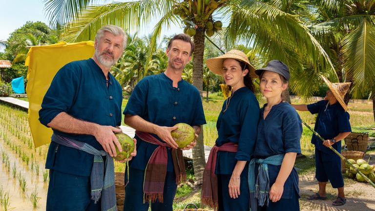 "Das Traumschiff - Phuket": Auf einer Kokosnussplantage: Max Parger (Florian Silbereisen), Martin Grimm (Daniel Morgenroth), Annika Ehler (Maxine Kazis) und Melly Sturm (Marija Mauer) stehen zusammen und blicken in die Ferne. Sie tragen traditionelle Bauernkleidung und die Frauen Hüte. Die Männer halten Kokosnüsse in den Händen.