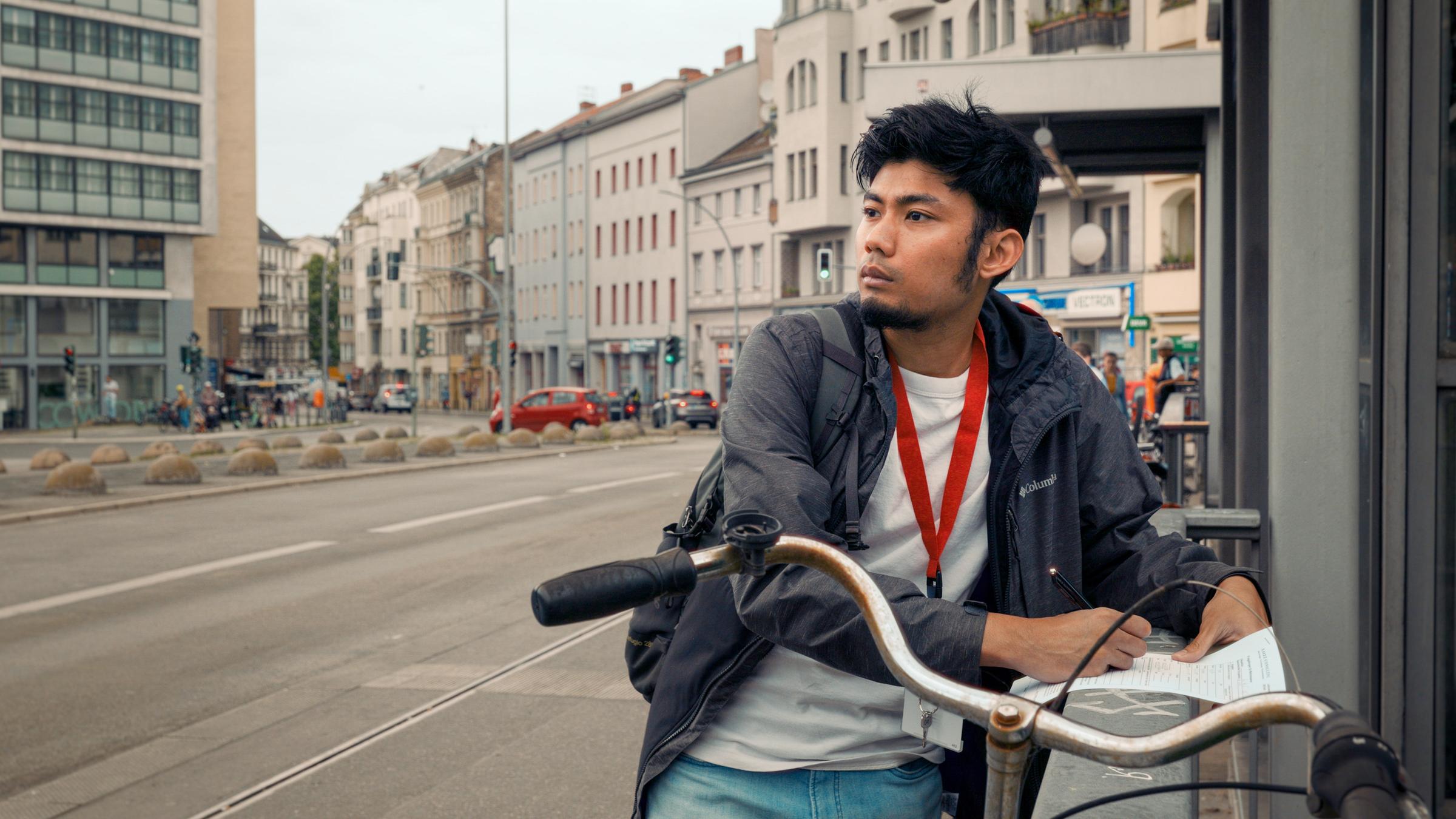 "Ab 18! - Großstadt Odysseus": Junger Mann steht an einem Geländer und macht sich auf einem Blatt Papier Notizen.