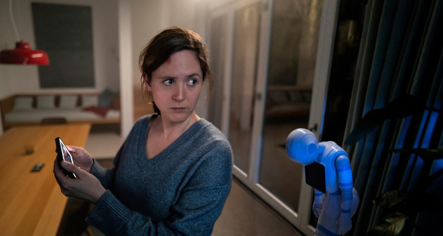 "Unsichtbarer Angreifer": Es ist dunkel im Haus und Emma (Emily Cox) ist offenbar allein. Auch Hausroboter Samy steht ausgeschaltet in der Ecke. Der Bildschirm auf Emmas Handy leuchtet, sie schaut besorgt um sich.