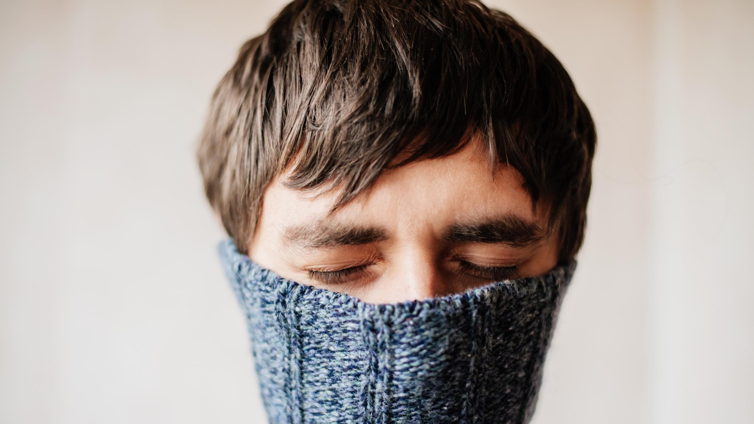 "Anders im Kopf - Neurodiversität als Stärke": Mann mit geschlossenen Augen versteckt sein Gesicht in einem Pullover.