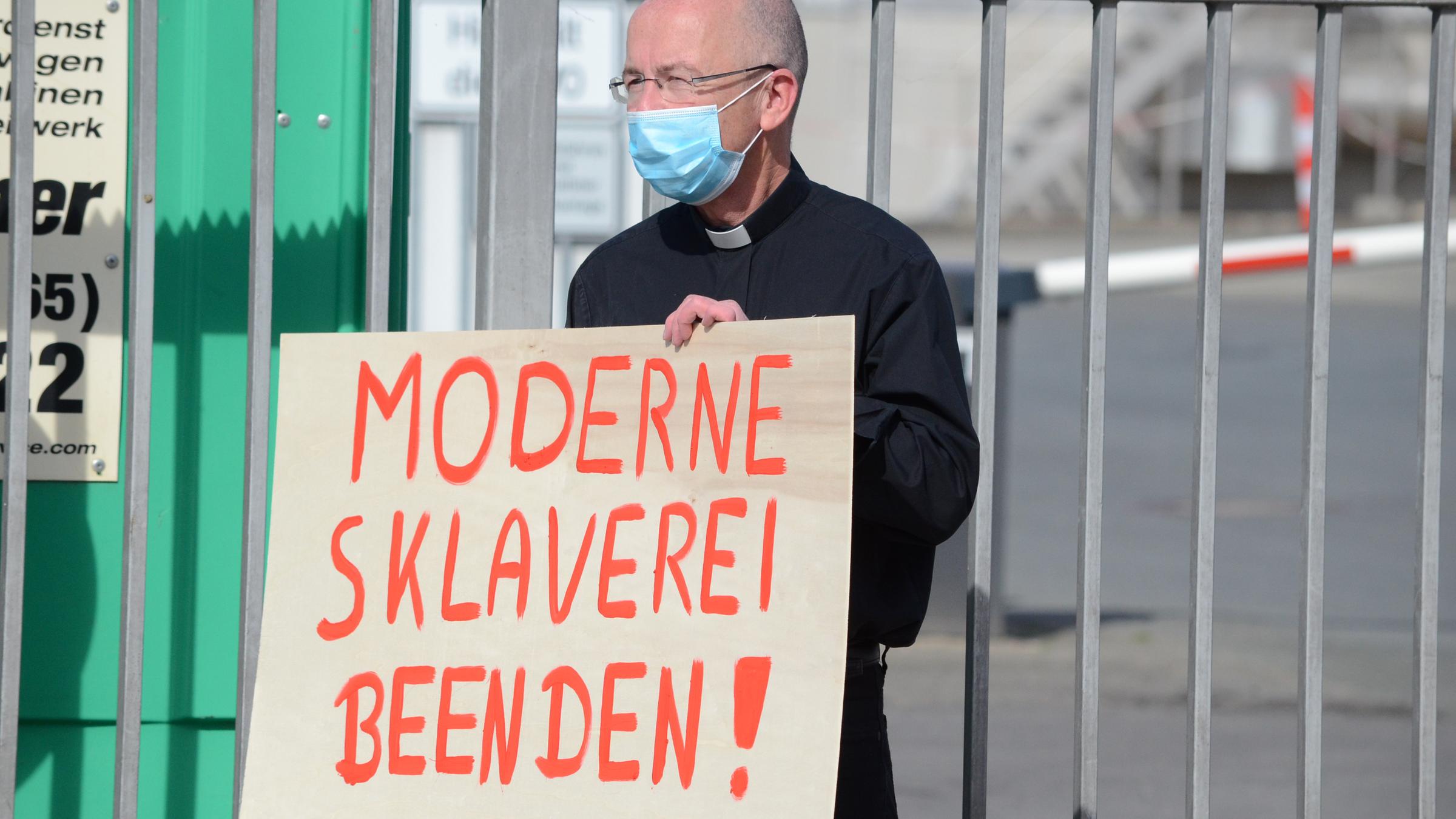 "Die Vergessenen - Kampf für Gerechtigkeit - Zum Auftakt des Katholikentages in Erfurt": Peter Kossen, ein katholischer Priester, steht mit einem Plakat mit der Aufschrift "Moderne Sklaverei beenden" vor einem Tor zu einer Fleischfabrik.