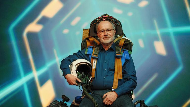 "Terra X: Zeit - Vermessung der Zeit - Mit Professor Harald Lesch": Harald Lesch sitzt auf einem Pilotensitz und schaut lächelnd in die Kamera.