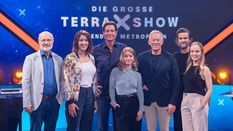 "Die große "Terra X"-Show - Legendäre Metropolen": Harald Lesch, Hannah Emde, Thomas Heinze, Karoline Schuch, Johannes B. Kerner, Tom Beck und Friederike Kempter stehen im Studio vor dem Sendungslogo und lächeln in die Kamera
