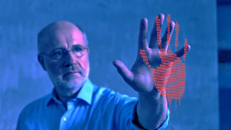"Terra X Harald Lesch ... und wie KI uns überwacht": Montage, blau verfremdet: Harald Lesch steht unscharf im Hintergrund, trägt ein Hemd und hat seine Hand nach vorne gestreckt. Die Handinnenfläche ist scharf und Richtung Kamera geöffnet. Über der Handfläche ist eine Grafik in Gestalt einer Hand mit roten Einsen und Nullen gelegt.