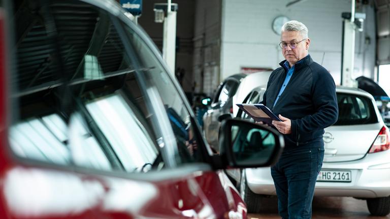 "Die Malocher: Wirtschaftskrise vor Ort": Im Verkaufsraum eines Autohauses steht Claus Trilling mit einem Klemmblock zwischen ausgestellten Autos.