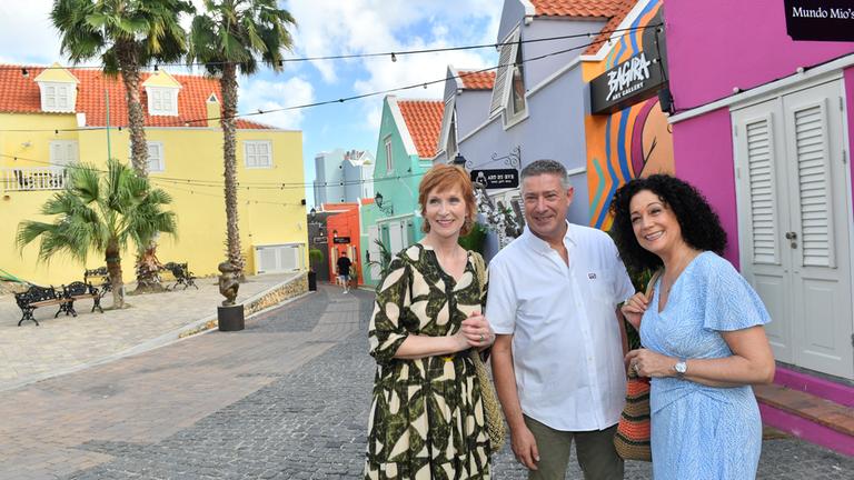 "Das Traumschiff: Curaçao": In der Stadt: Vor bunten Häusern steht Jochen Thabazi (Joachim Llambi) umringt von Hanna Liebhold (Barbara Wussow) und Birgit Schneider (Fanny Stavjanik). Sie unterhalten sich lachend.