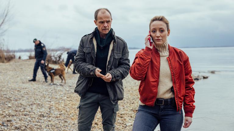 "Die Toten vom Bodensee - Die Medusa": Micha Oberländer (Matthias Koeberlin) und Luisa Hoffmann (Alina Fritsch) stehen zusammen am Ufer. Luisa Hoffmann (Alina Fritsch) telefoniert mit dem Handy.