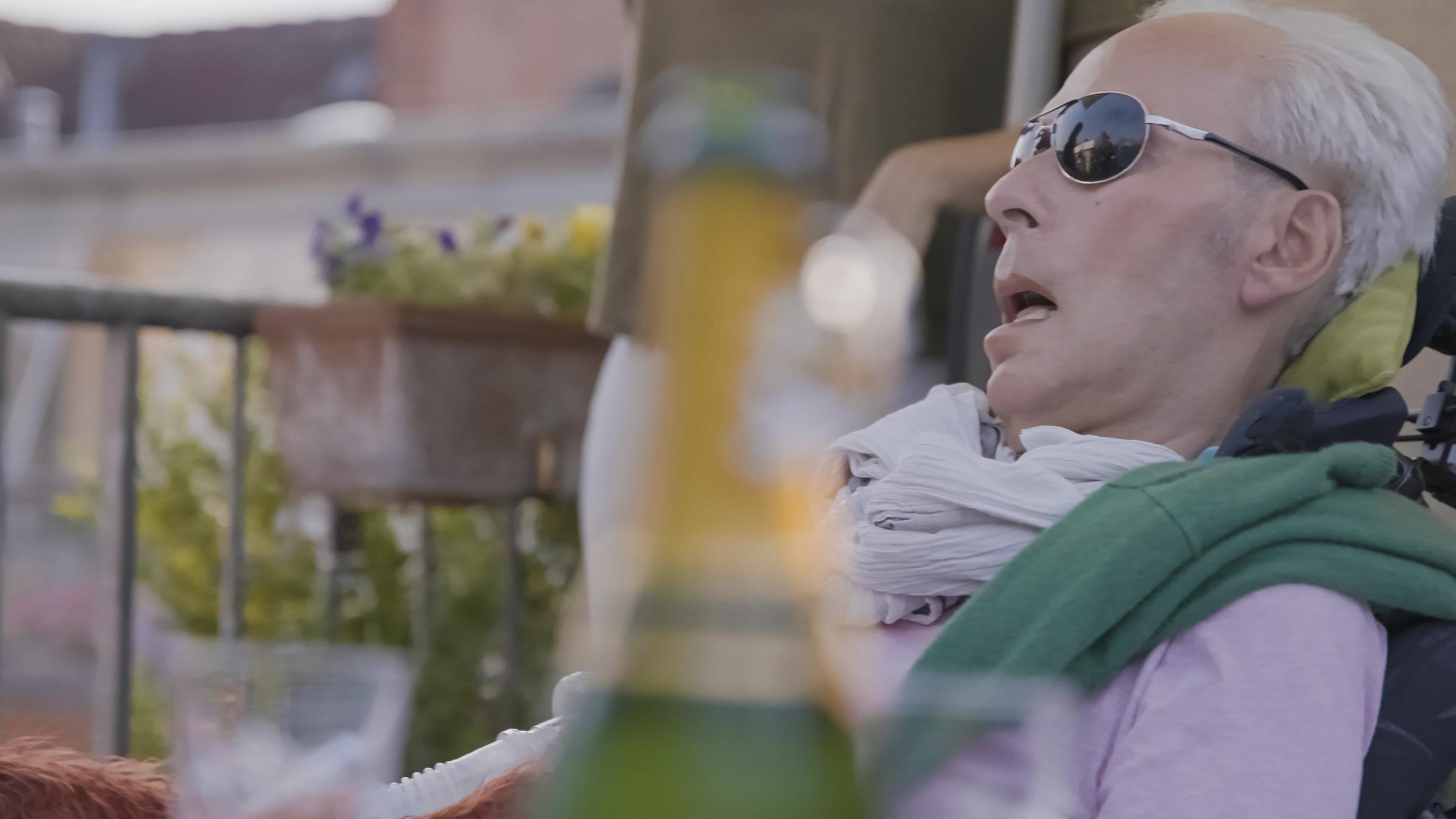 37° Mein Wille geschehe - Wie weit geht die moderne Medizin?": Benedict Mülder liegt auf der Terrasse. Er trägt eine dunkle Sonnenbrille, ein fliederfarbenes Hemd und hat einen grünen Pullover um die Schultern gelegt.