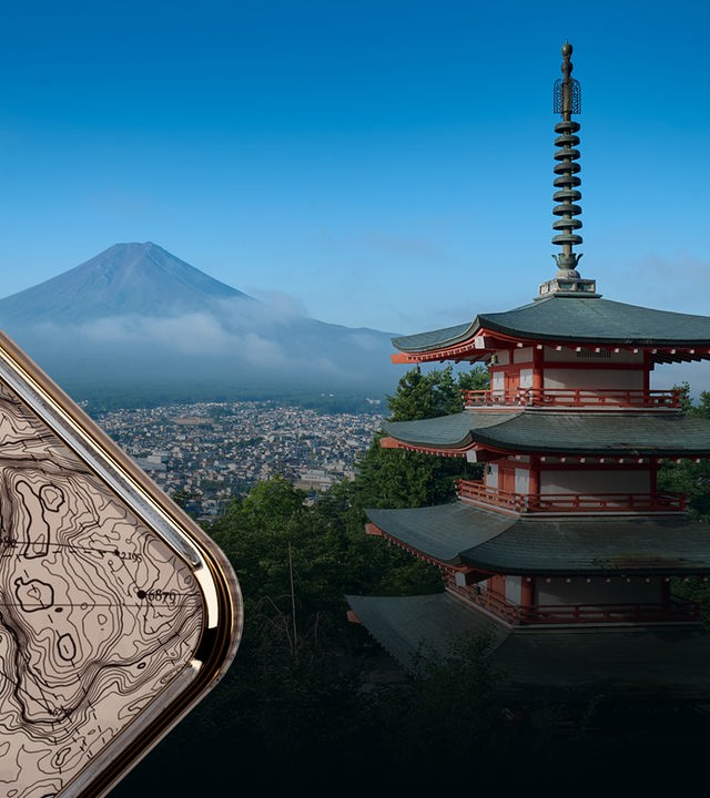Im Hintergrund der Fuji, in der Mitte Nebel über einer Stadt. Im Vordergrund: Die Chureito Pagode, ein rot-weißes Gebäude mit vier übereinander gestaffelten, grünen Dachflächen.