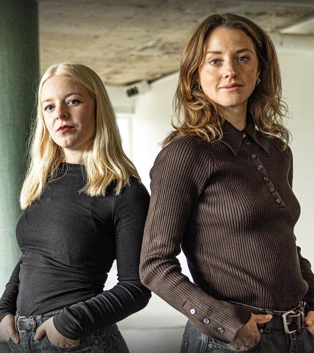 Zwei junge Frauen stehen mit den Händen in den Hosentaschen nebeneinander.