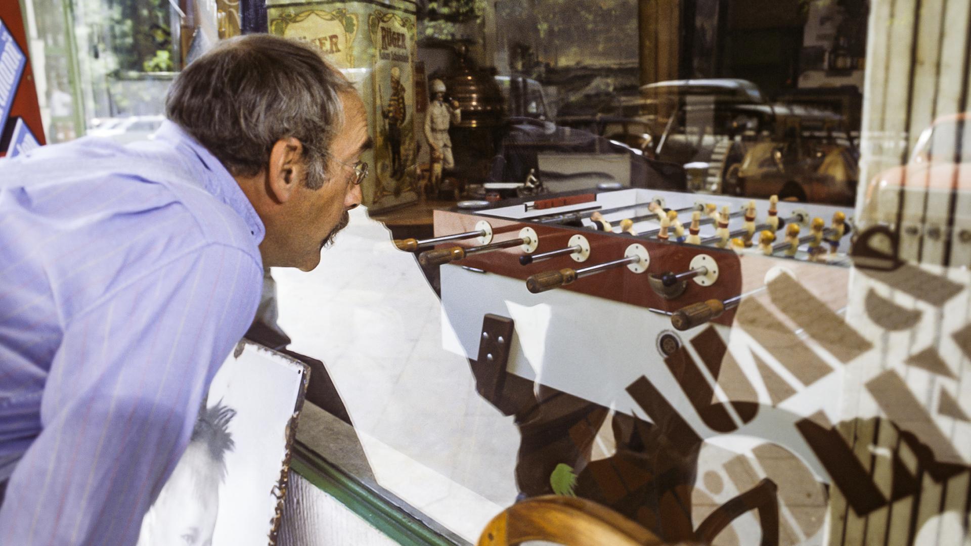 Peter schaut durch ein Schaufenster, hinter dem ein Tischkicker zu sehen ist.