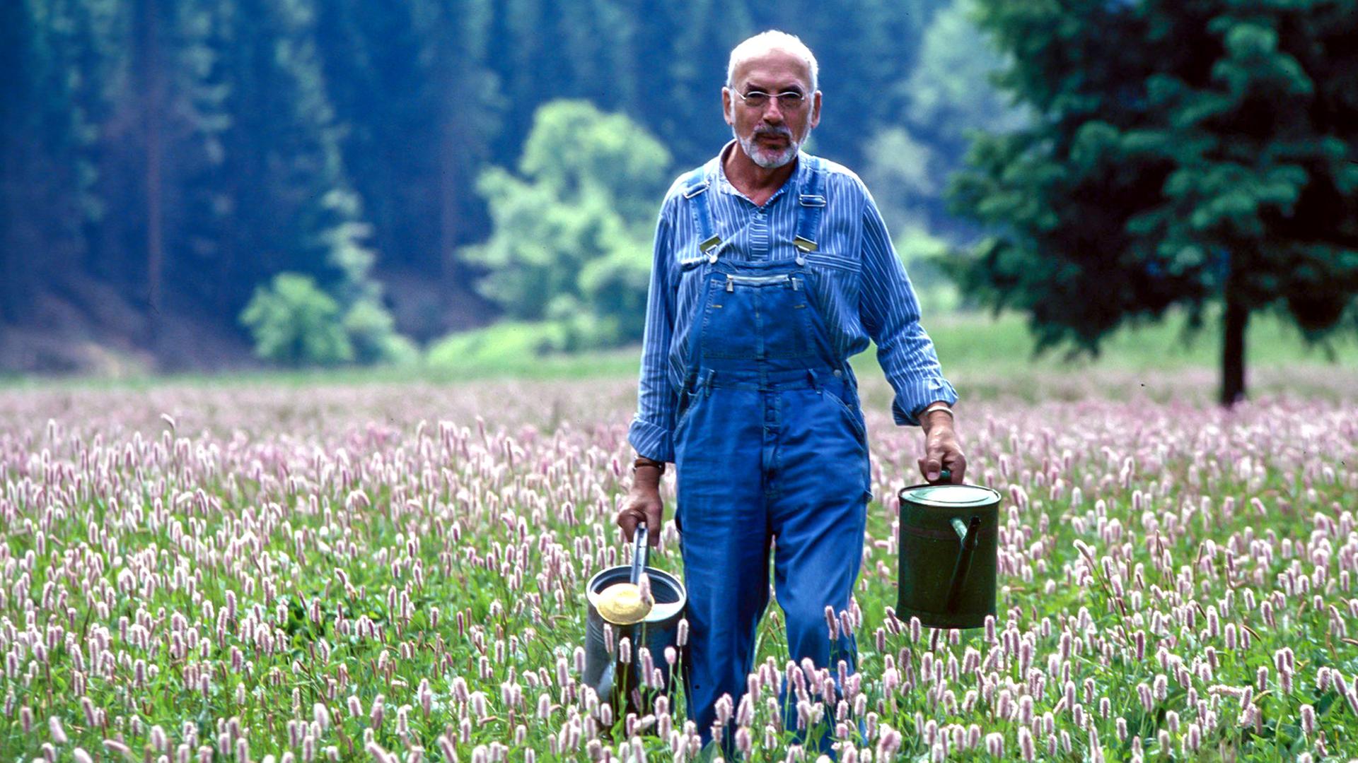 Peter Lustig geht mit einer Gieskanne über eine Wiese