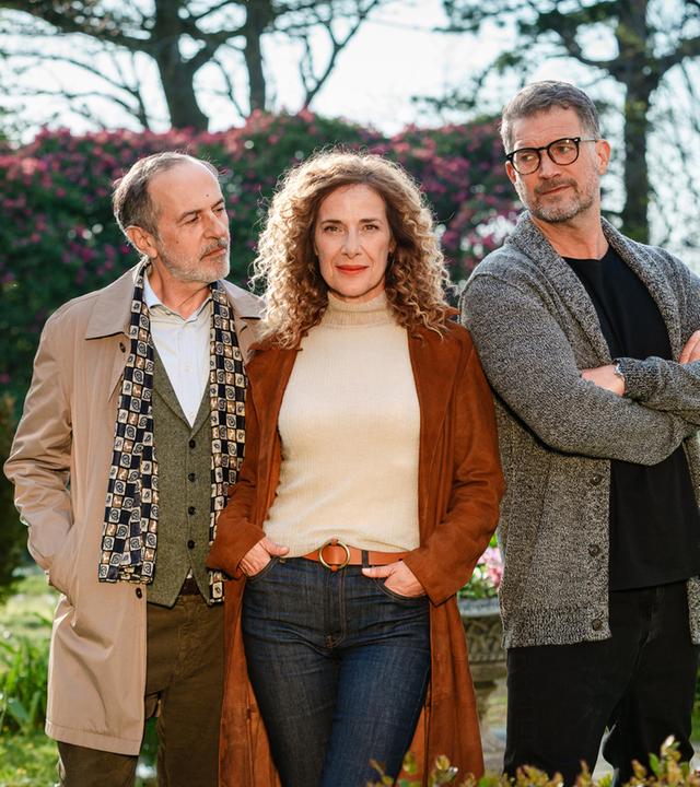 "Rosamunde Pilcher: Wo Liebe aufhört und wo sie beginnt": In einem Garten mit blühenden Pflanzen: Kate Evans (Clelia Sarto) steht in der Mitte zwischen Andrew Evans (Simon Böer) und Yamen Nicholls (Merab Ninidze)