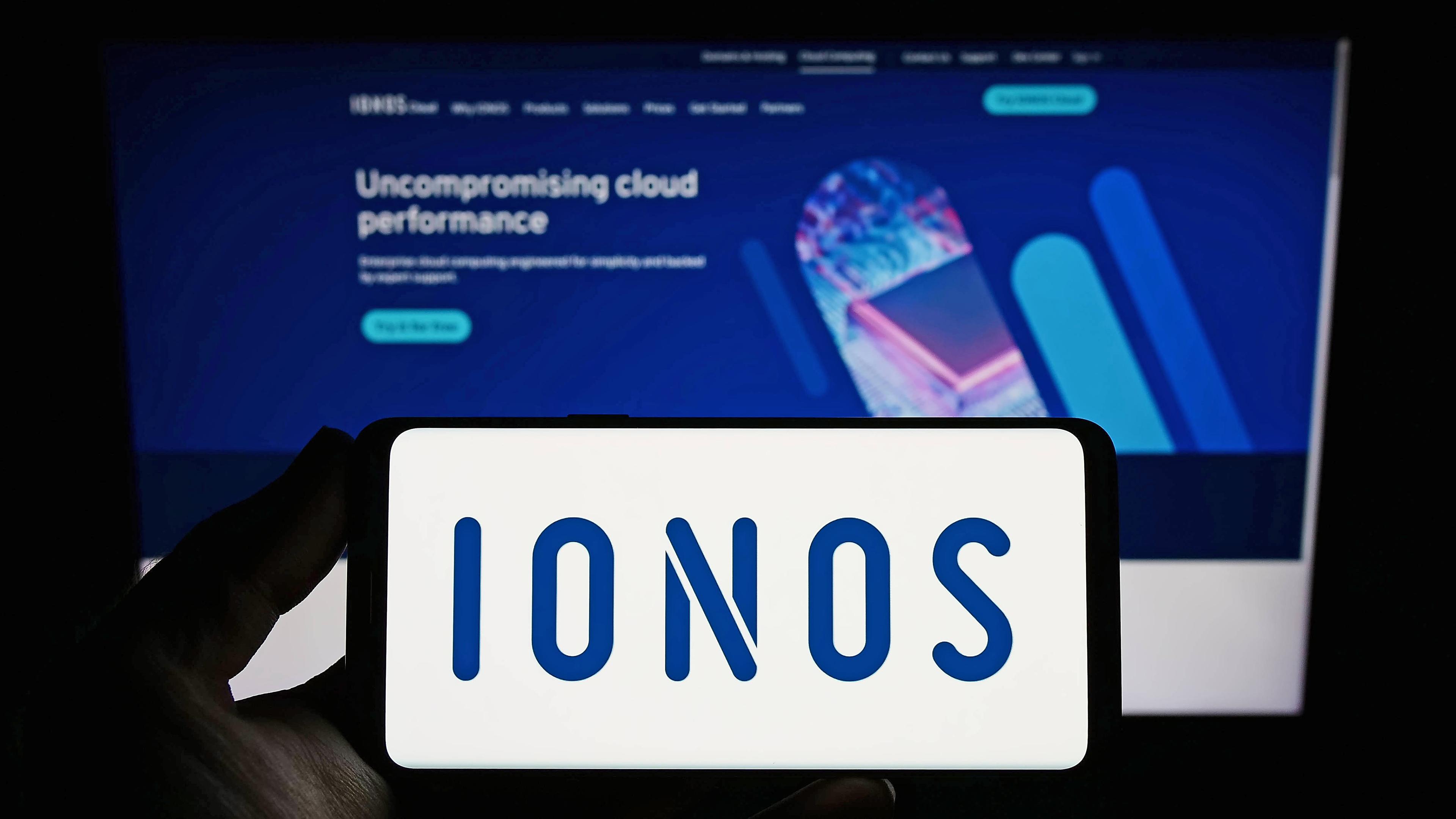 Person hält ein Smartphone mit dem Logo des deutschen Webhosting-Unternehmens Ionos SE auf dem Bildschirm