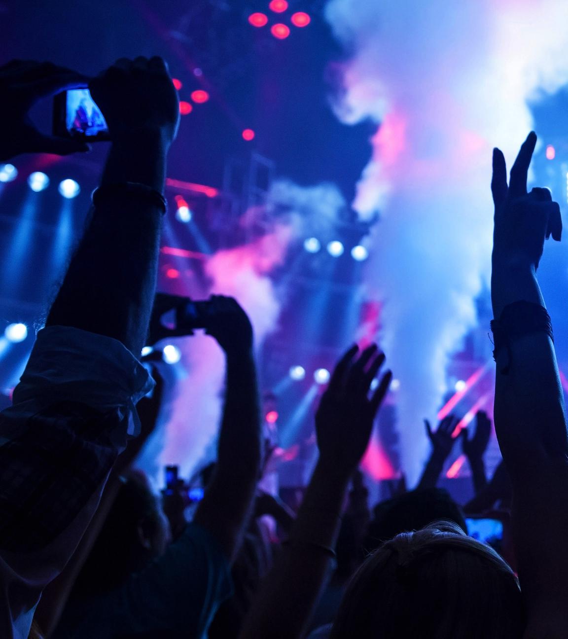 Eine tanzende Menge hebt ihre Arme in den Dunst einer Diskothek empor