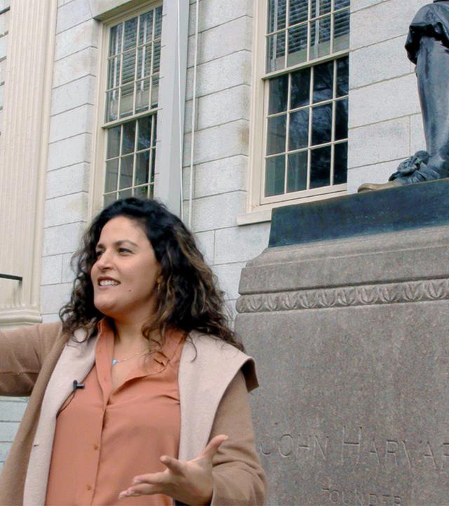 Eine Frau steht vor einem großen kassizistischen Gebäude mit einer Statue vor dem Eingang und macht ein Selfie.