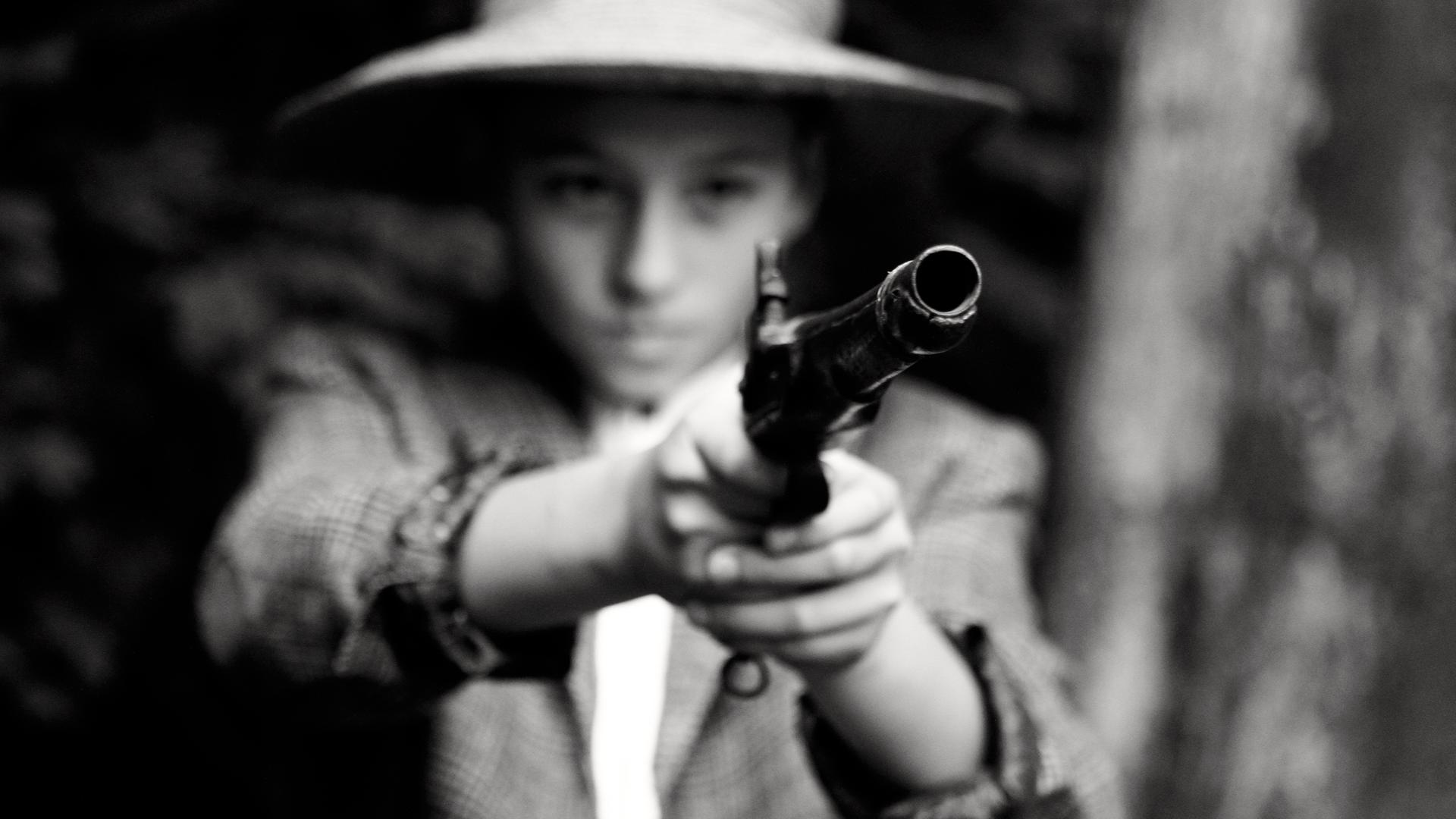 Nachgestellte Szene. Unscharfes Schwarz-Weiß-Foto: Ein Kind mit Hut hält einen altmodischen Revolver in beiden Händen.
