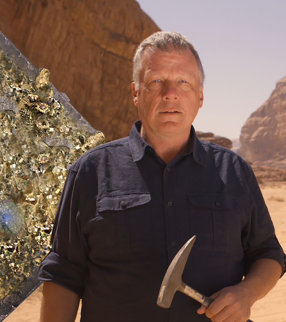 Colin Devey steht mit einem Hammer in der Hand im Sand vor einer Felsformation in der jordanischen Wüste.