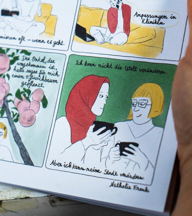 Nahaufnahme einer Comicseite mit zwei Frauen, eine mit rotem Kopftuch, die andere mit blonden Haaren und Brille, beide halten Tassen. Der Text lautet: „Ich kann nicht die Welt verändern. Aber ich kann meine Stadt verändern.“