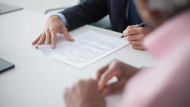 Hände unterschreiben einen Vetrag auf einem Schreibtisch