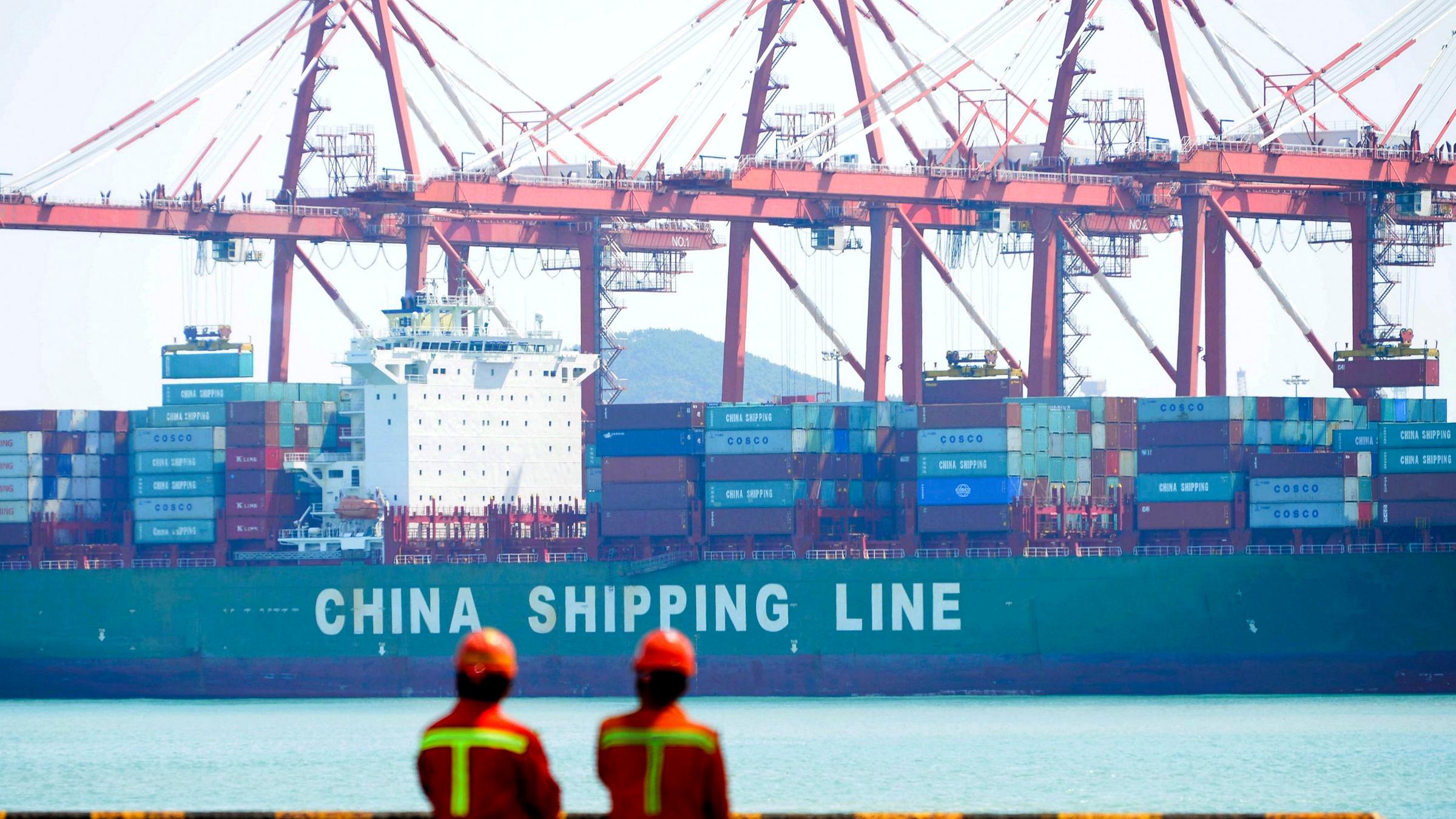 Hafenmitarbieter betrachten ein Containerschiff mit der Aufschift "China Shipping Line" 