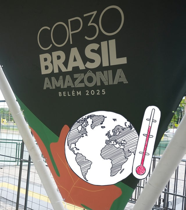 Auf dem Bild ist ein Plakat der Weltklimakonferenz COP30 zu erkennen. Daneben ist eine Weltkugel mit Termometer zu sehen.
