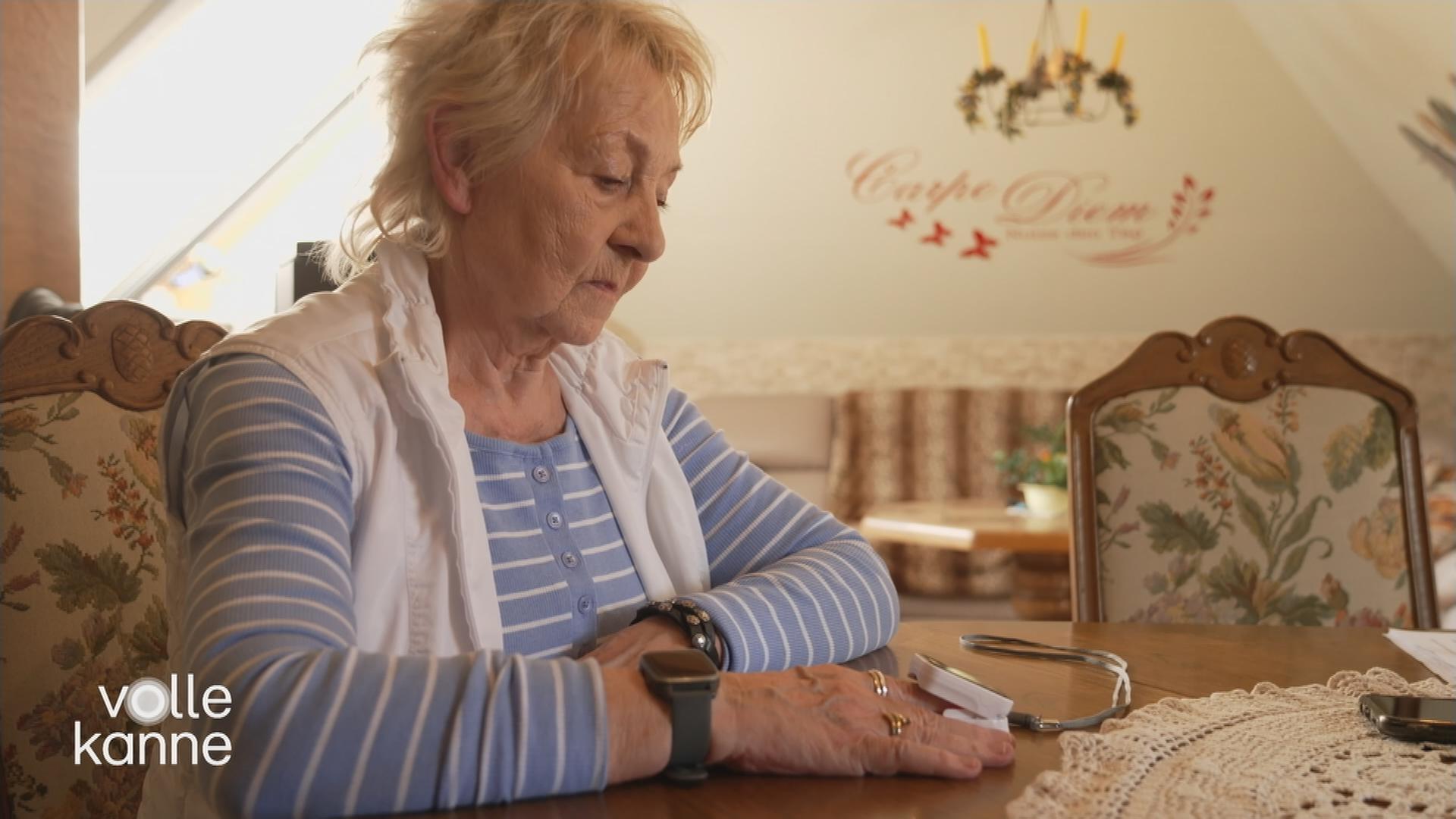 Eine Frau sitzt am Tisch und blickt auf das Sauerstoffmessgerät an ihrem Finger.