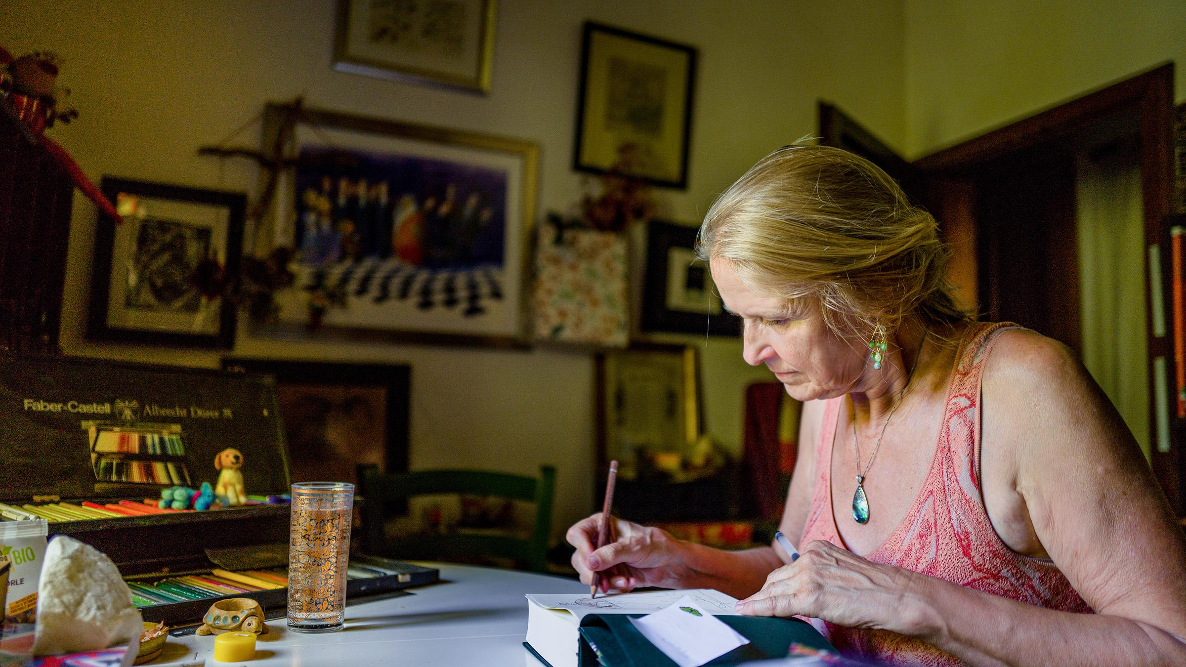 Frau sitzt am Schreibtisch und schreibt in ein Buch.