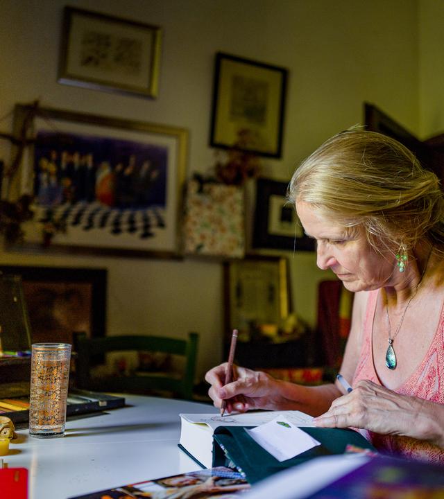 Frau sitzt am Schreibtisch und schreibt in ein Buch.