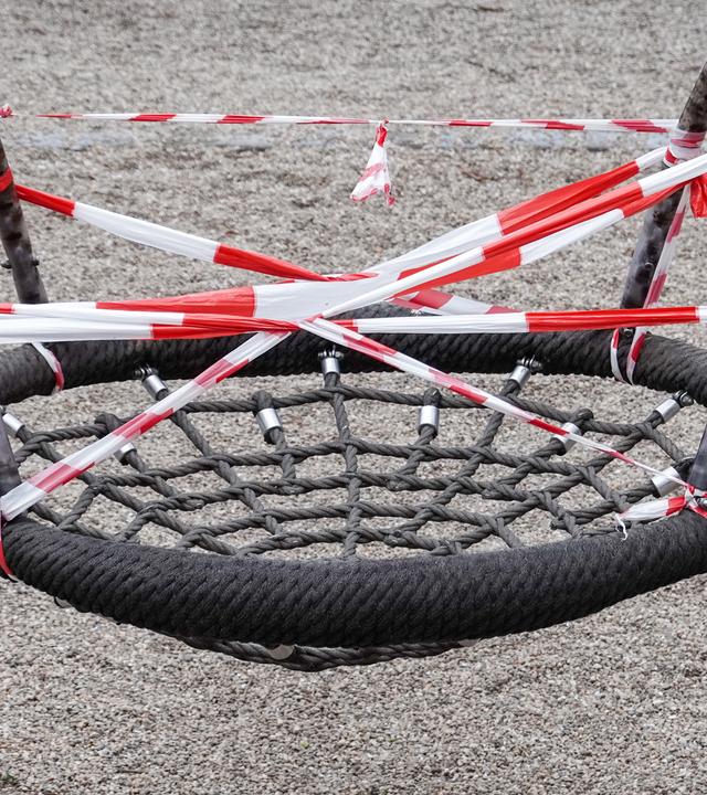 Sachsen, Leipzig: Eine Nestschaukel auf einem gesperrten Spielplatz im Leipziger Rosenthal ist mit rot-weißem Flatterband umwickelt