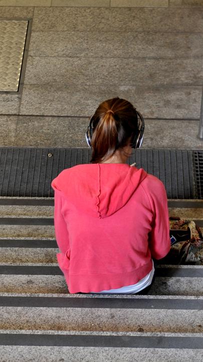 Ein Mädchen sitzt alleine auf der Treppe und hört Musik. 